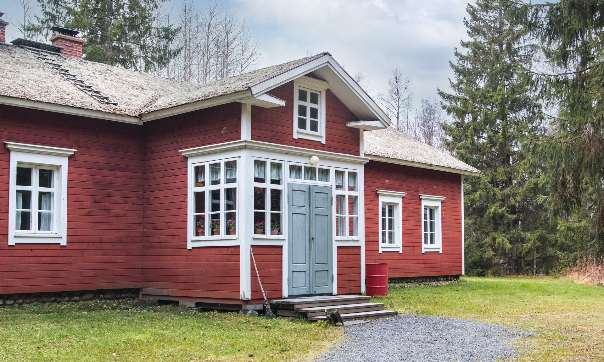 Ulkokuva, Yli-Juuruksen perinteinen punaiseksi maalattu puutalo, jossa vaaleat ikkunanpielet ja pieni kuisti, ympärillä puita ja nurmikkoa.