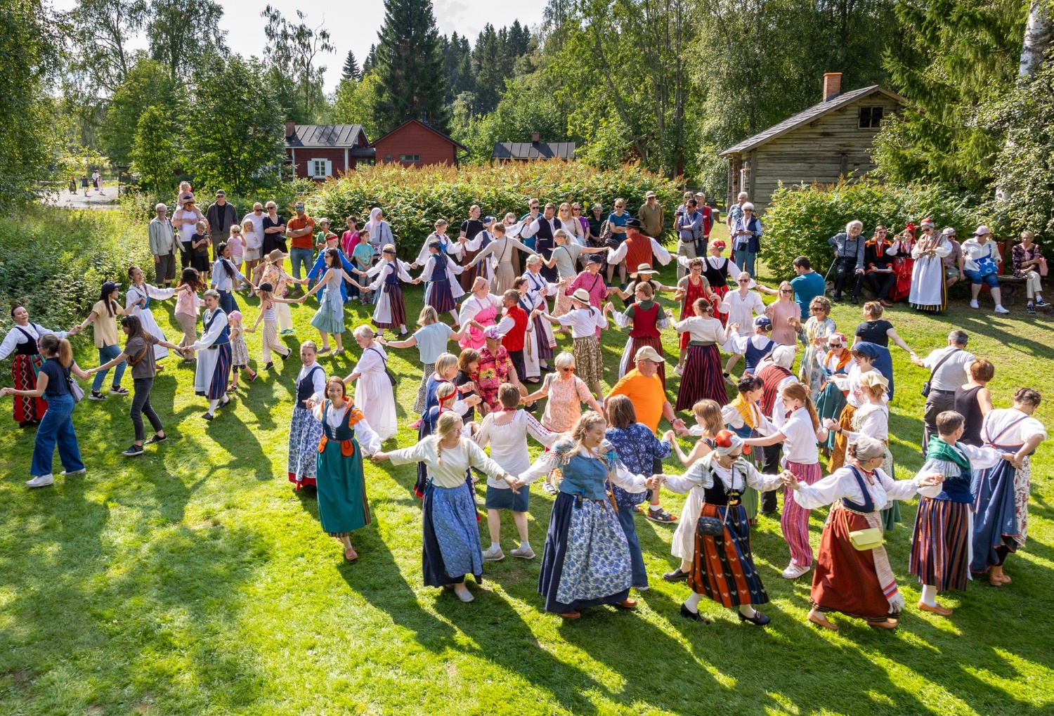 Perinneasuihin pukeutuneita ihmisiä tanssii ketjumuodostelmassa nurmikolla.